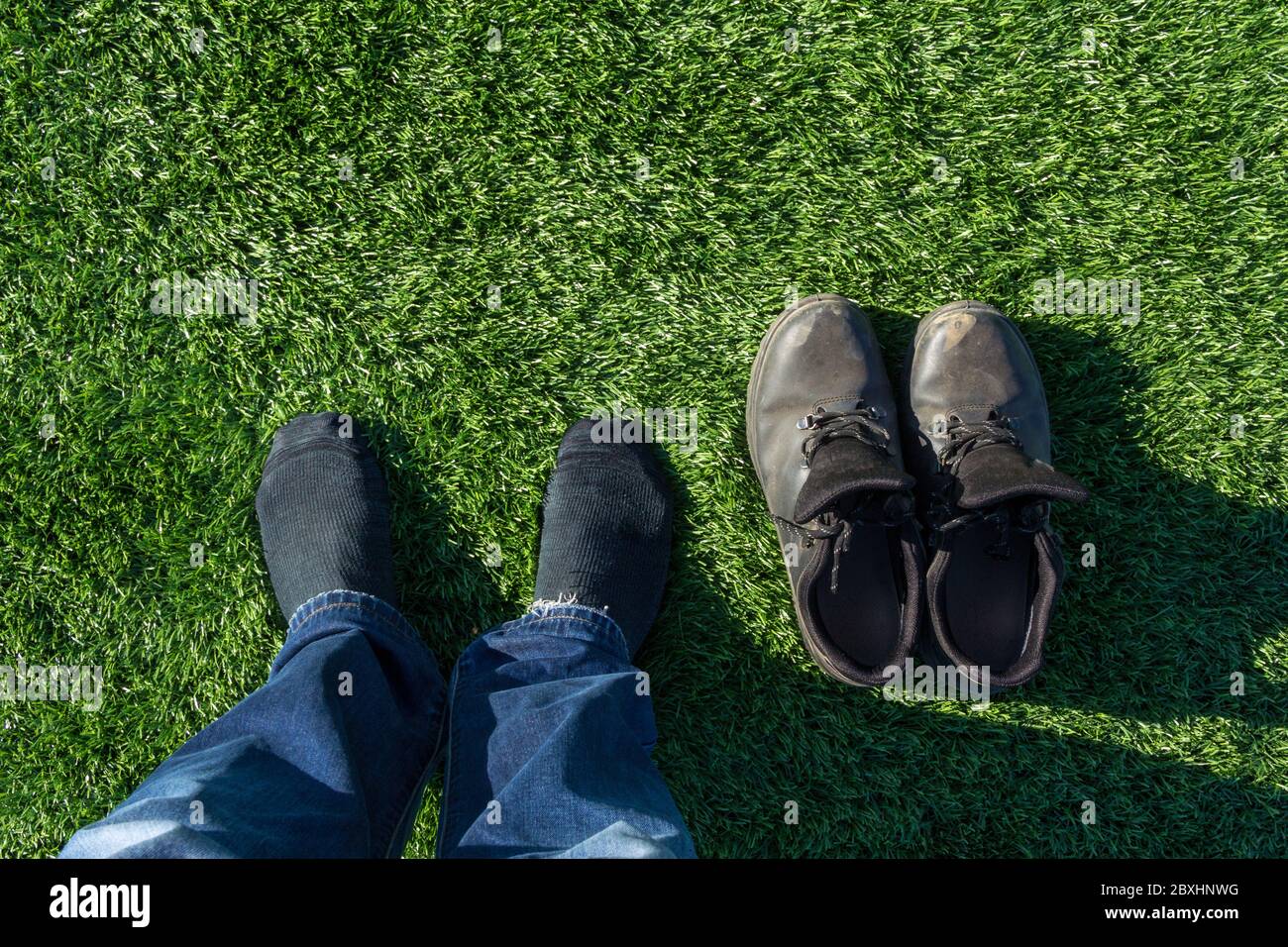 Legs of a worker without shoes on a soccer field. The man took off his shoes and stood on the football field in socks. Green grass and white border li Stock Photo