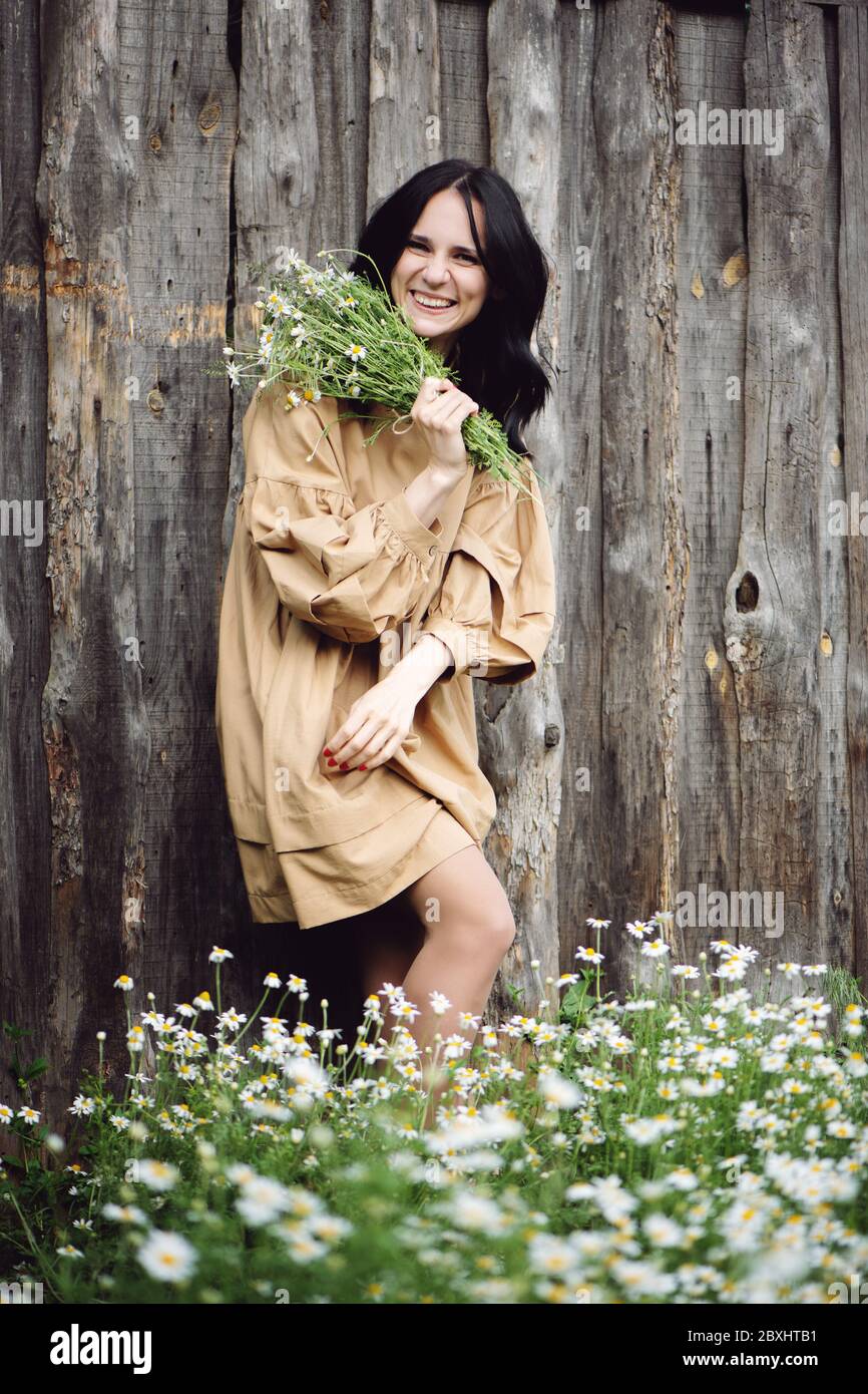 Smiling woman holding bouquet of chamomile in hands near the fence. Stock Photo