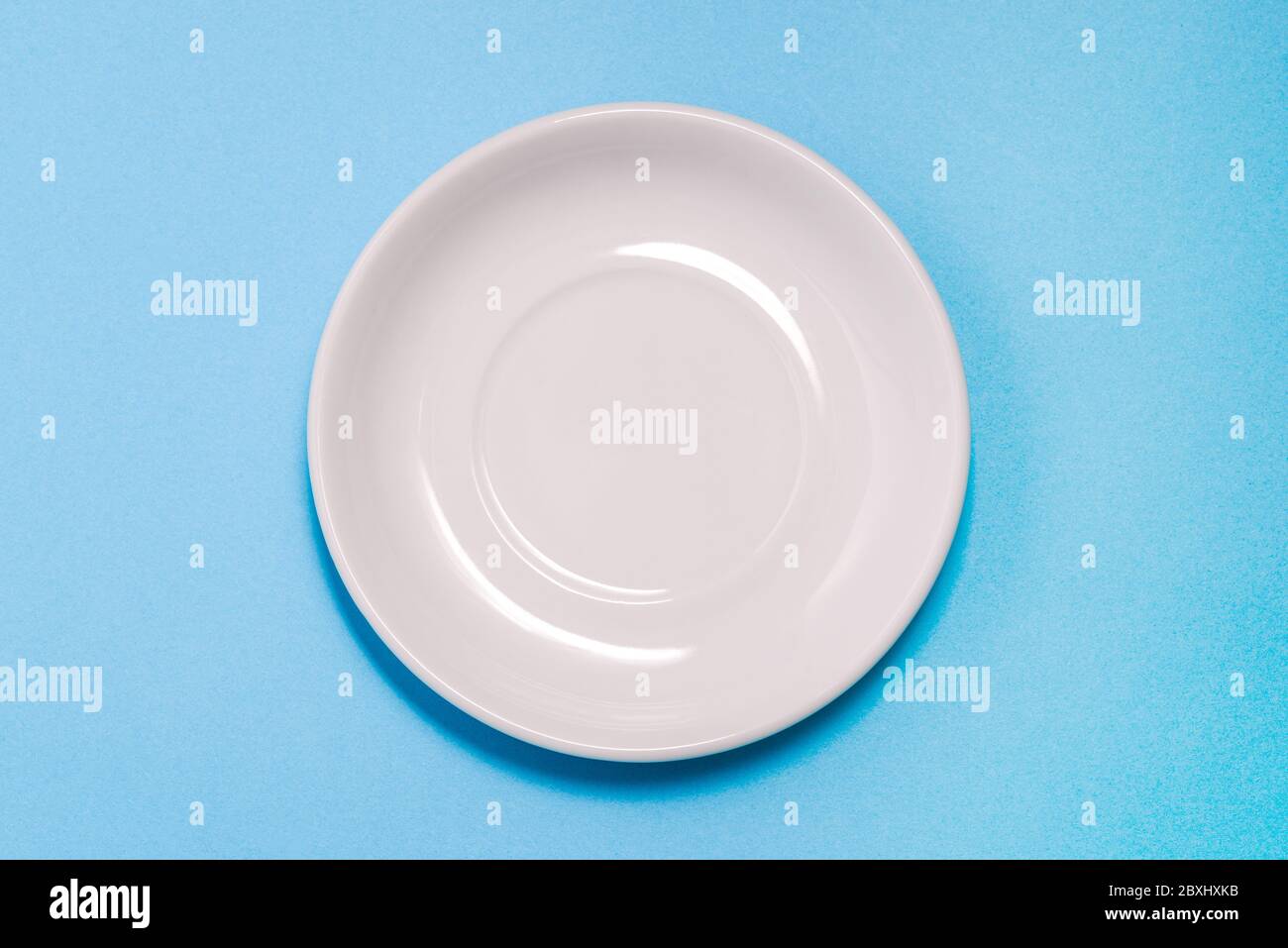 An empty white plate on a blue background. Clean dishes for Breakfast, dinner or lunch. Kitchen items. A top view of a flat layout. Stock Photo