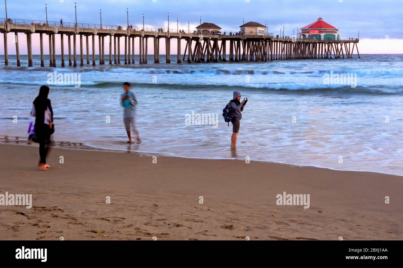 The iconic Huntington Beach pier at sunset, with three people enjoying