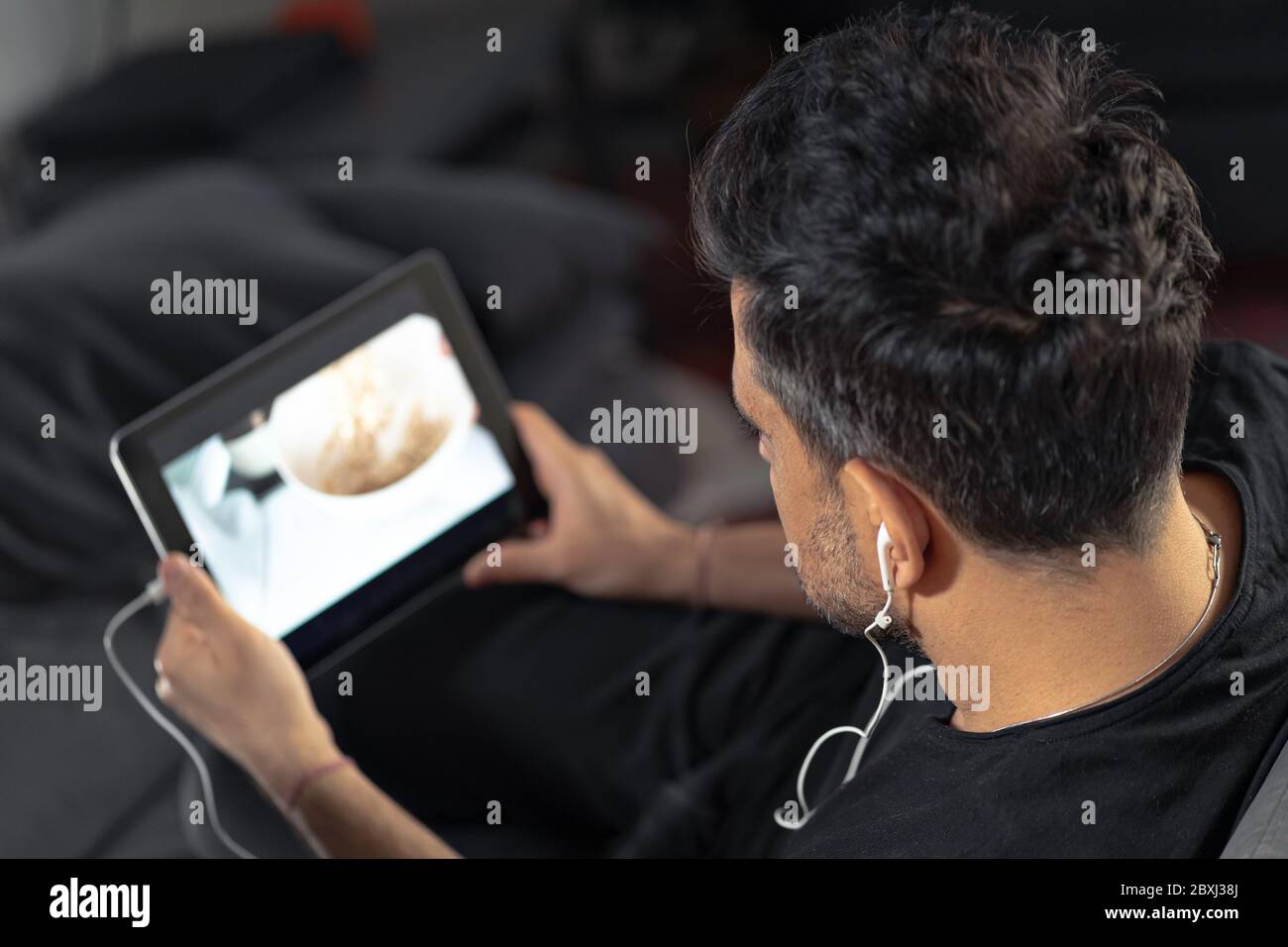 man hand holding using digital tablet watching online cooking master class using headphones. learning cooking remotely Stock Photo