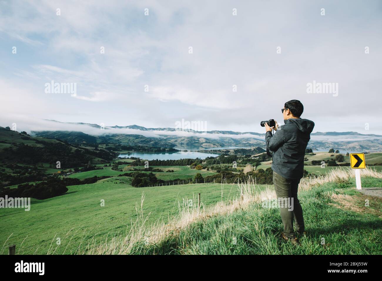 Asian tourist man photographer with camera taking pictures in mountains on foggy weather day. Stock Photo