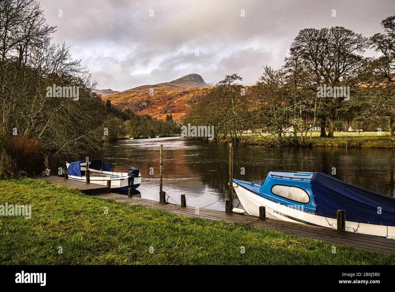 Two boats moored at the private jetty on River Dochart in Killin, with one of the peaks of the Tarmachan ridge in the background. Stock Photo