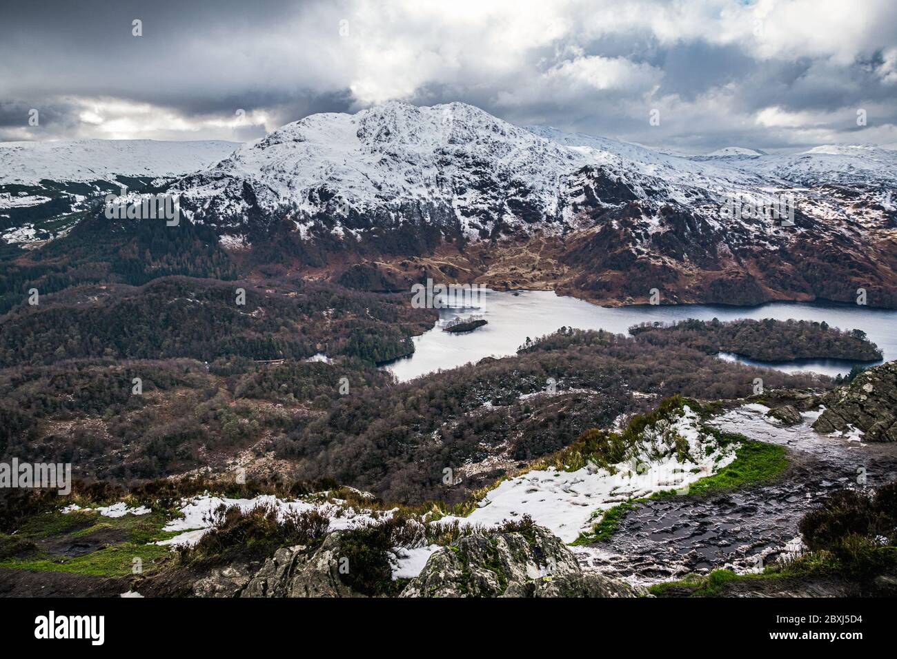 Winter Scottish view from Ben A'an overlooking Loch Katrine and snow-capped peak of Ben Venue in Scottish Highlands. Stock Photo