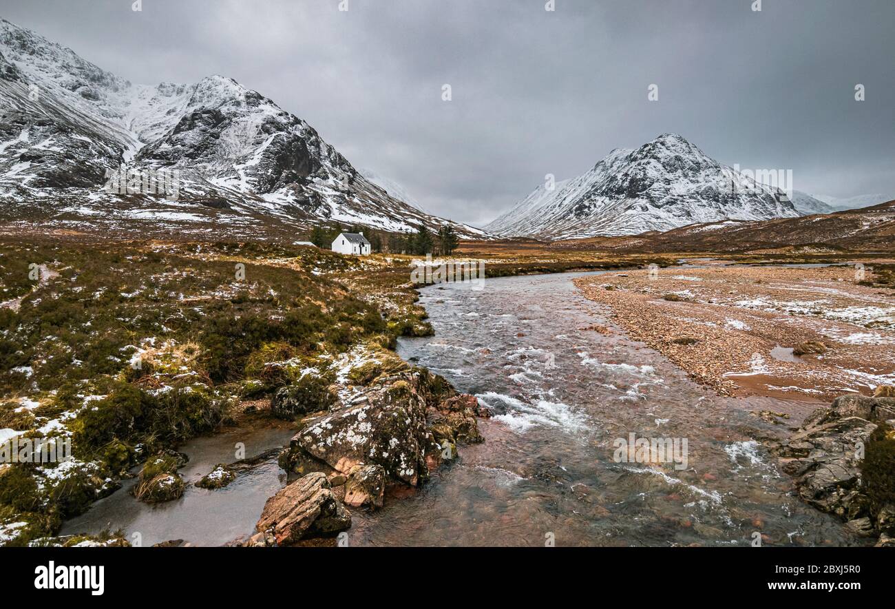 Picturesque winter landscape of Glen Coe with the iconic white cottage against the backdrop of Buachaille Etive Mor and stormy clouds on the horizon. Stock Photo