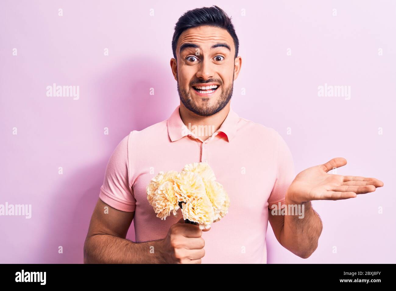 Young handsome romantic man with beard holding bouquet of flowers over ...