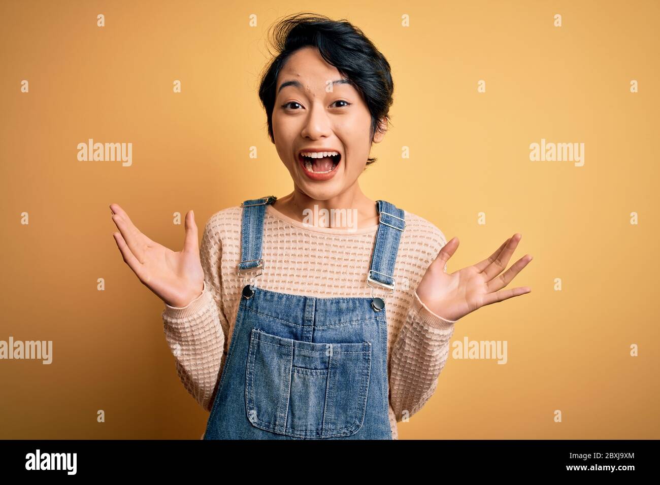 Young beautiful asian girl wearing casual denim overalls over isolated ...