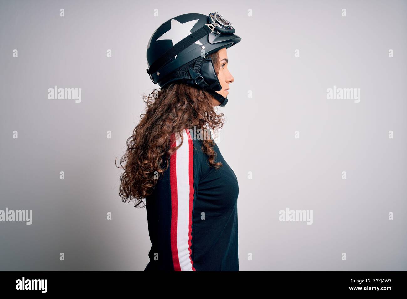 Beautiful motorcyclist woman with curly hair wearing moto helmet over white  background looking to side, relax profile pose with natural face with conf  Stock Photo - Alamy