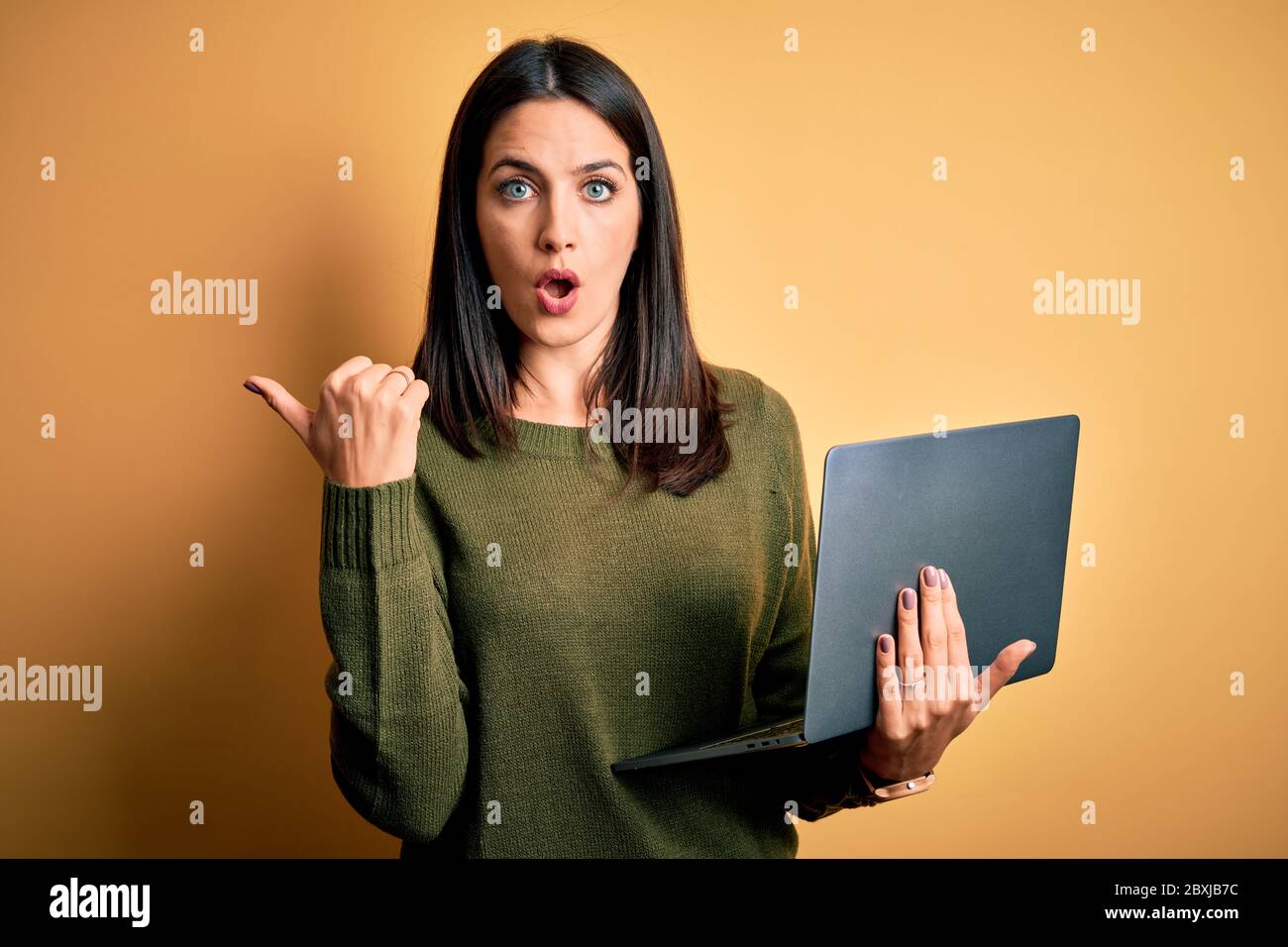 Young brunette woman with blue eyes working using computer laptop over ...