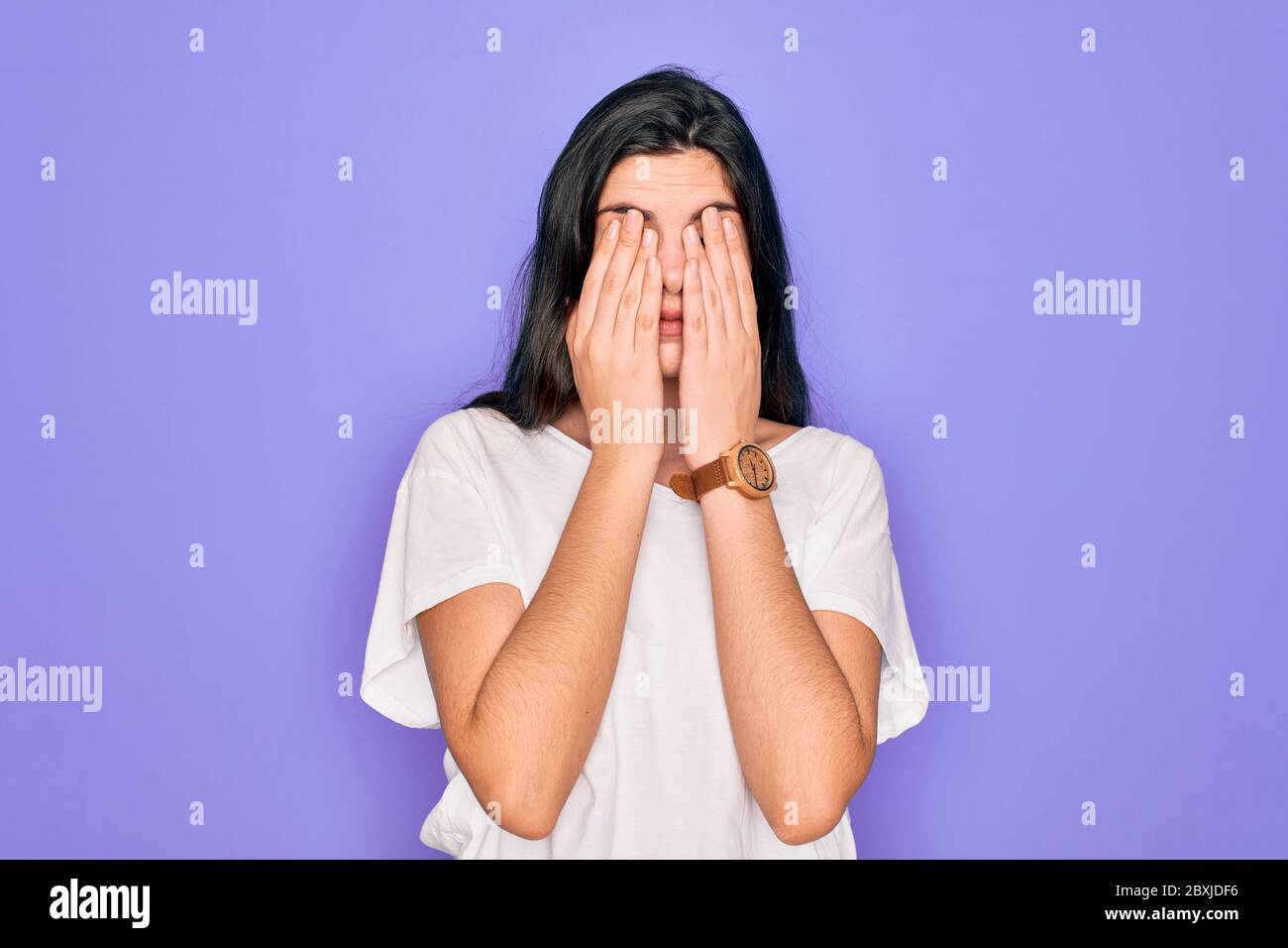 Young beautiful brunette woman wearing casual white t-shirt over purple background rubbing eyes for fatigue and headache, sleepy and tired expression. Stock Photo