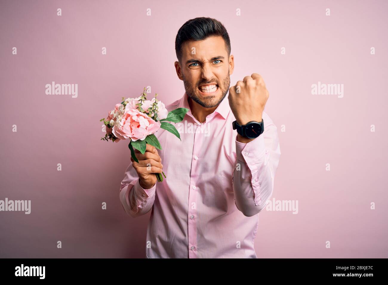 Young romatic man holding bouquet of spring flowers over pink isolatd ...