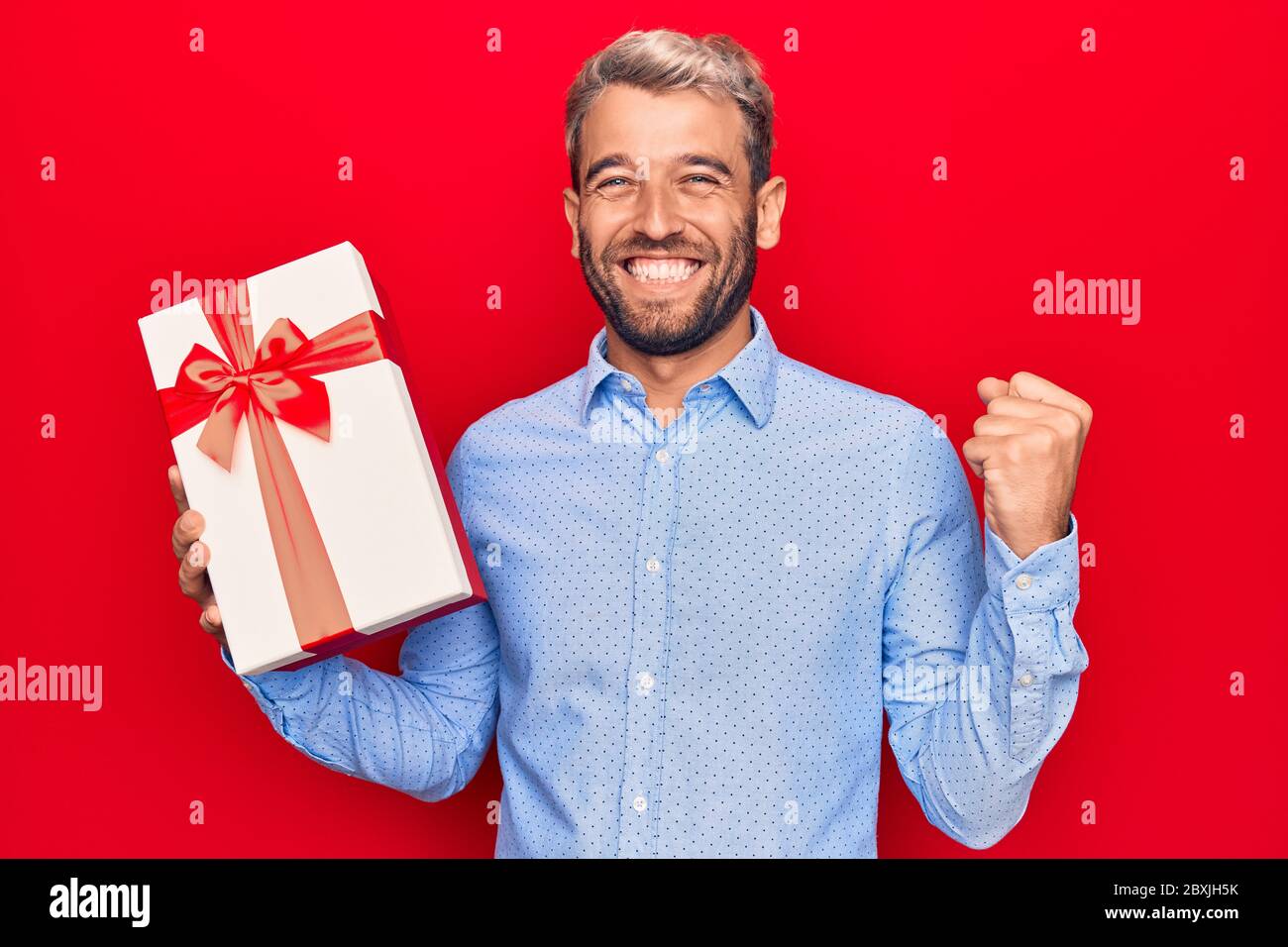 Young handsome blond man with beard holding birthday present over ...