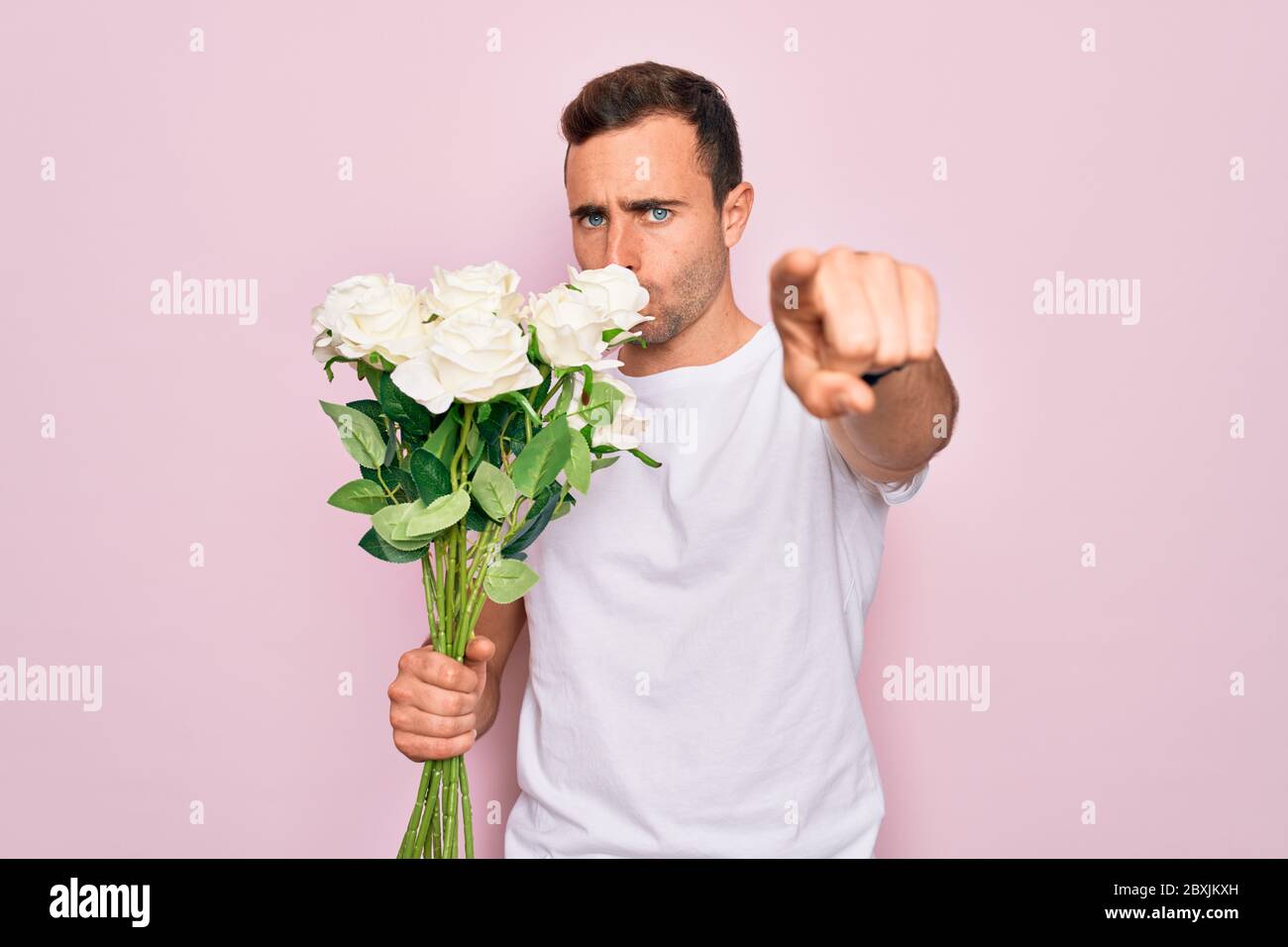 Young handsome man with blue eyes holding bouquet of flowers over pink ...