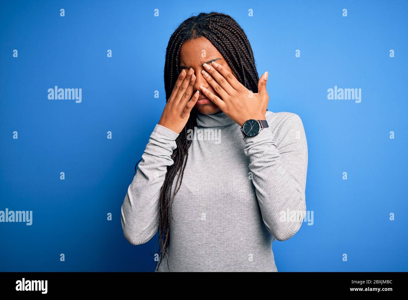 Young african american woman standing wearing casual turtleneck over blue isolated background rubbing eyes for fatigue and headache, sleepy and tired Stock Photo