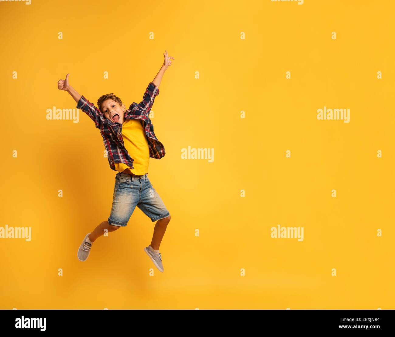 Happy and emotional child jumps over a yellow background. Stock Photo