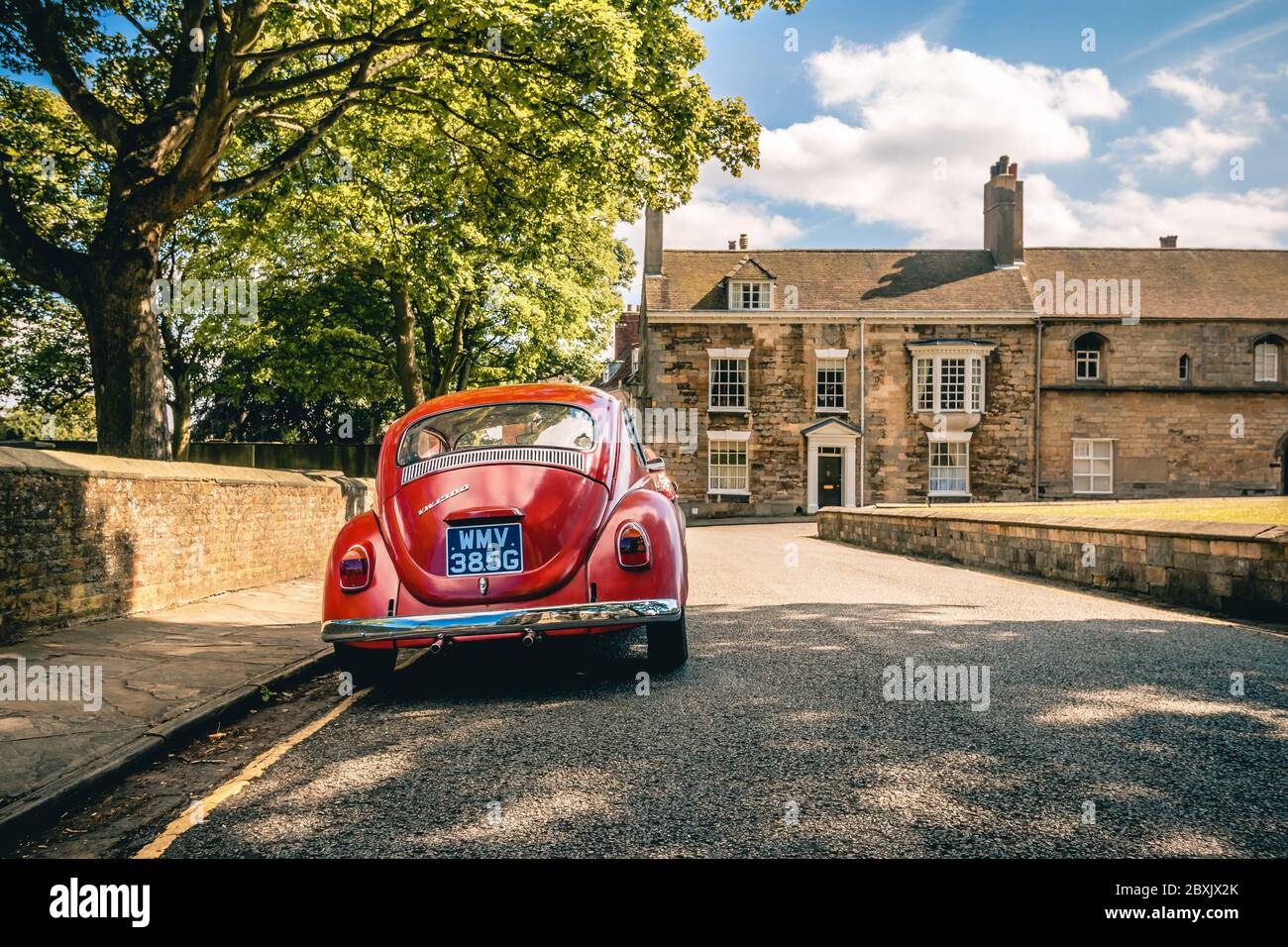 Lincoln - 01 July 2017 - Vintage Red VW Beetle with Traditional English Stone Cottage in Lincoln, UK Stock Photo