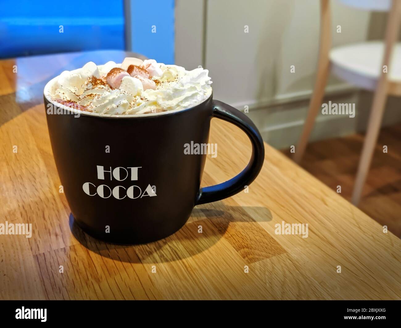 Nice Cup of Hot Chocolate with Fresh Cream and Marshmallows on Wooden Bench in Cafe, UK Stock Photo