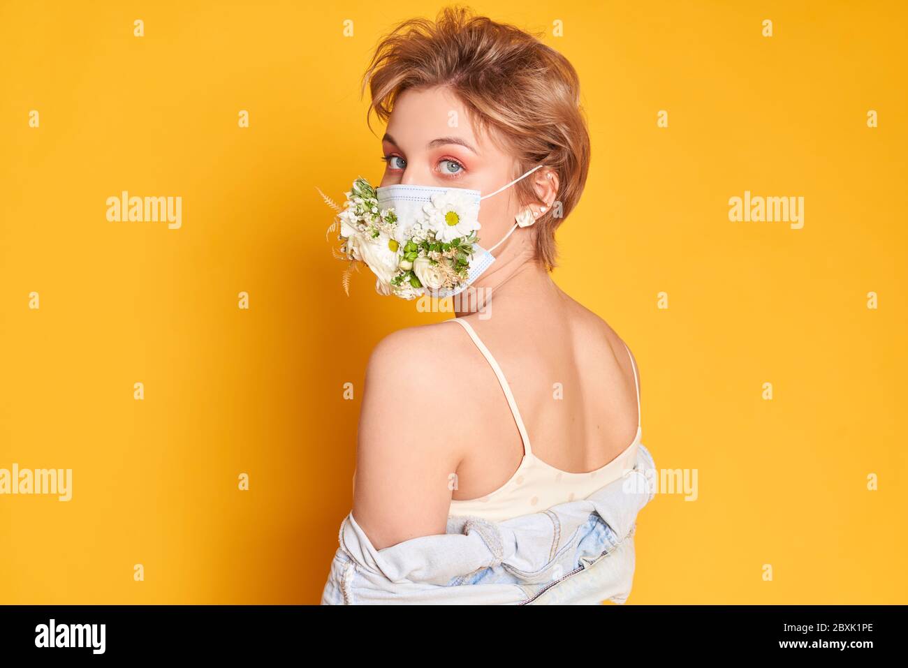 Face mask design with flowers. Portrait of beautiful woman with blue eyes, fashion make-up and mask on the orange background Stock Photo