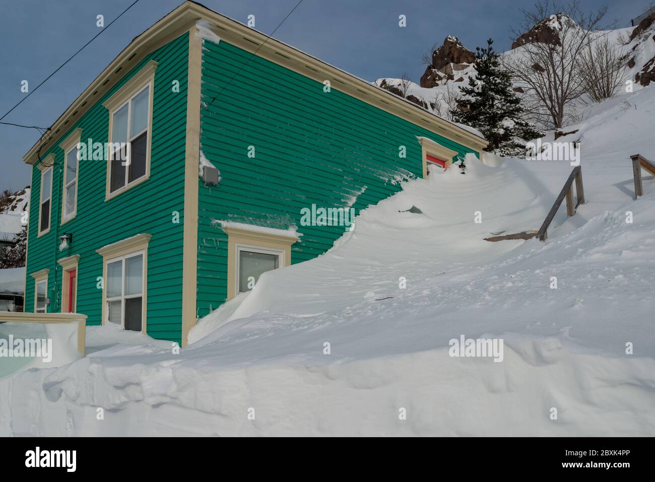 Exterior corner of a green wooden building with narrow clapboard and cream coloured trim. The windows are double hung. There's drifts of snow. Stock Photo