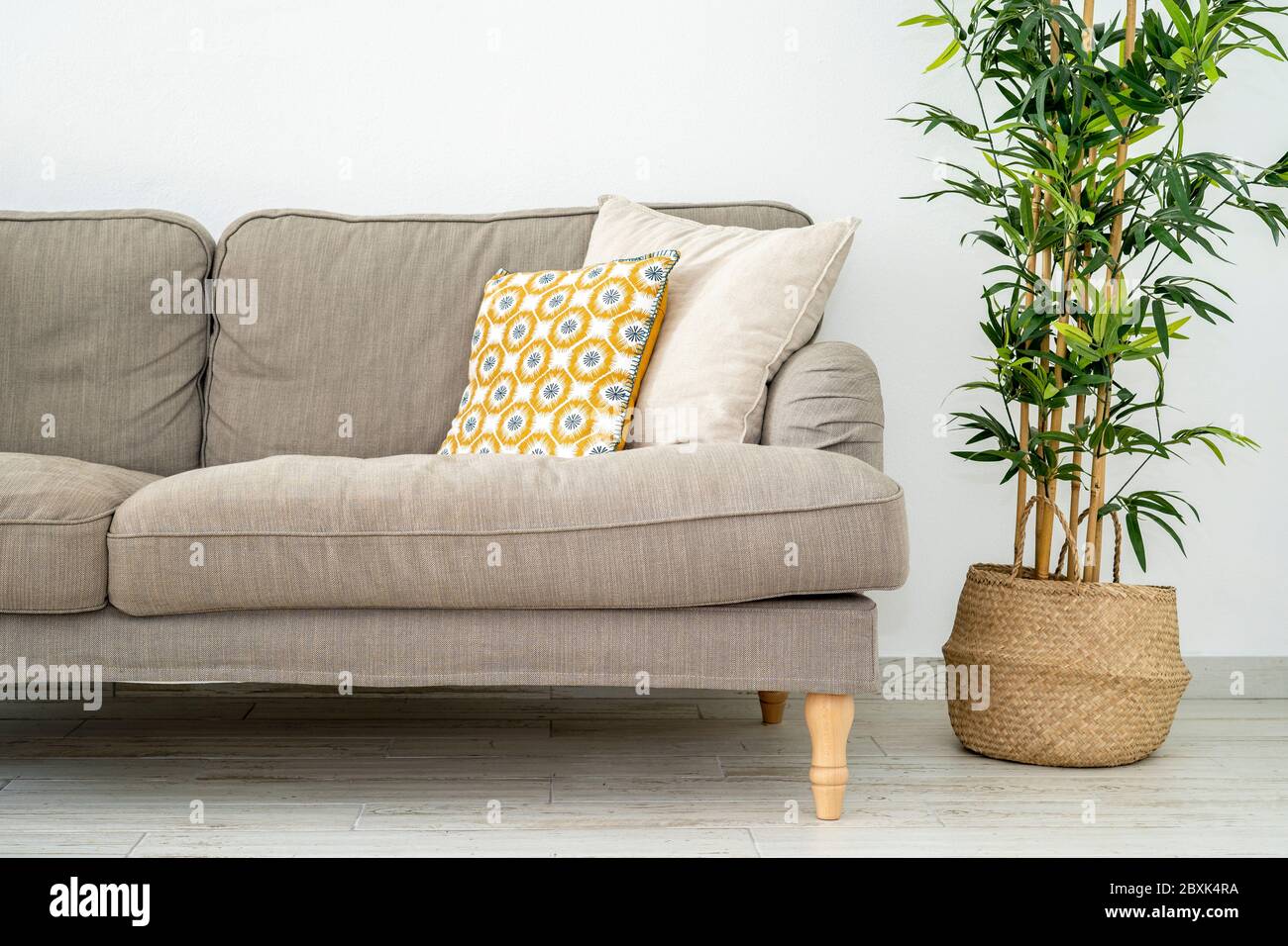 On the corner of the living room a sofa with green plant on the side. Yellow pillow on gray couch. Modern interior contemporany style living room. Stock Photo