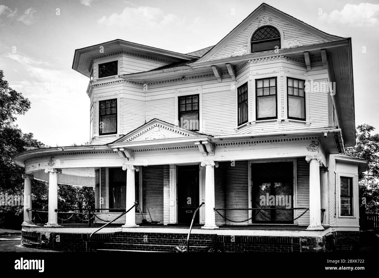 An aging home, designed in stylized Greek revival with Queen Ann elements, with it's wrap around porch and chain link swag railing accents in St. Clou Stock Photo