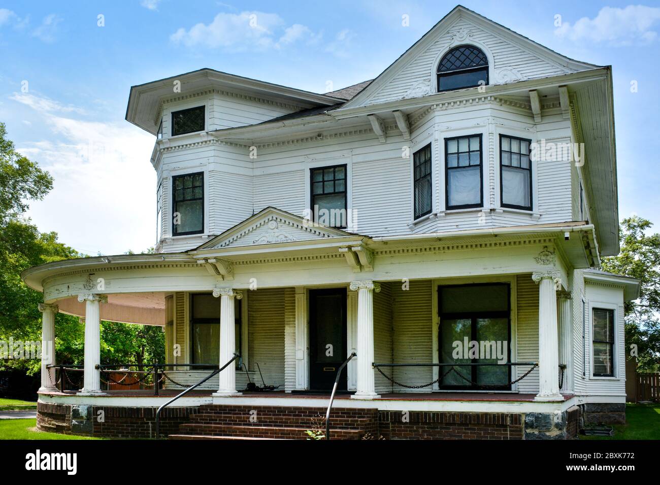 An aging home, designed in stylized Greek revival with Queen Ann elements, with it's wrap around porch and chain link swag railing accents in St. Clou Stock Photo