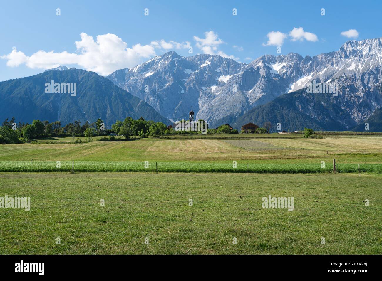 Green meadows along the rocky mountain range with typical small Austrian church at sunny summer day, Mieming, Austria Stock Photo