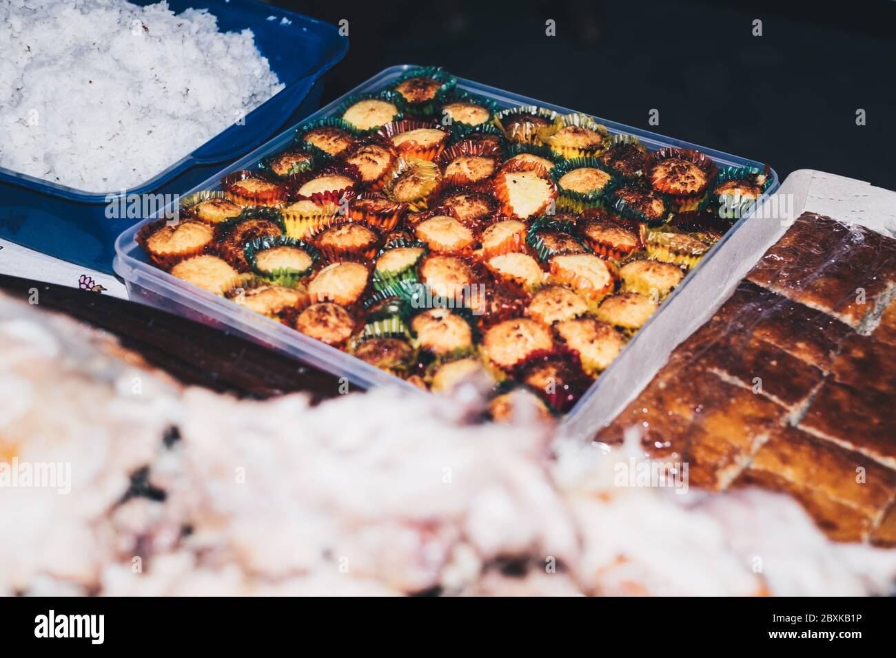 Filipino desserts on the table - in full view is the rectangular clear plastic container of coconut macaroons in colorful paper cups. Stock Photo