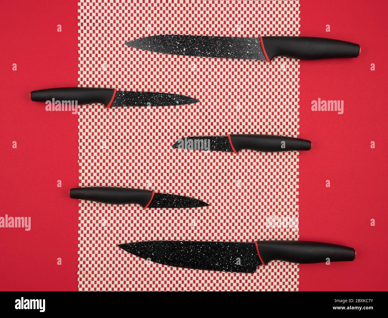 A set of kitchen knives on a white doily on a red background. Stock Photo