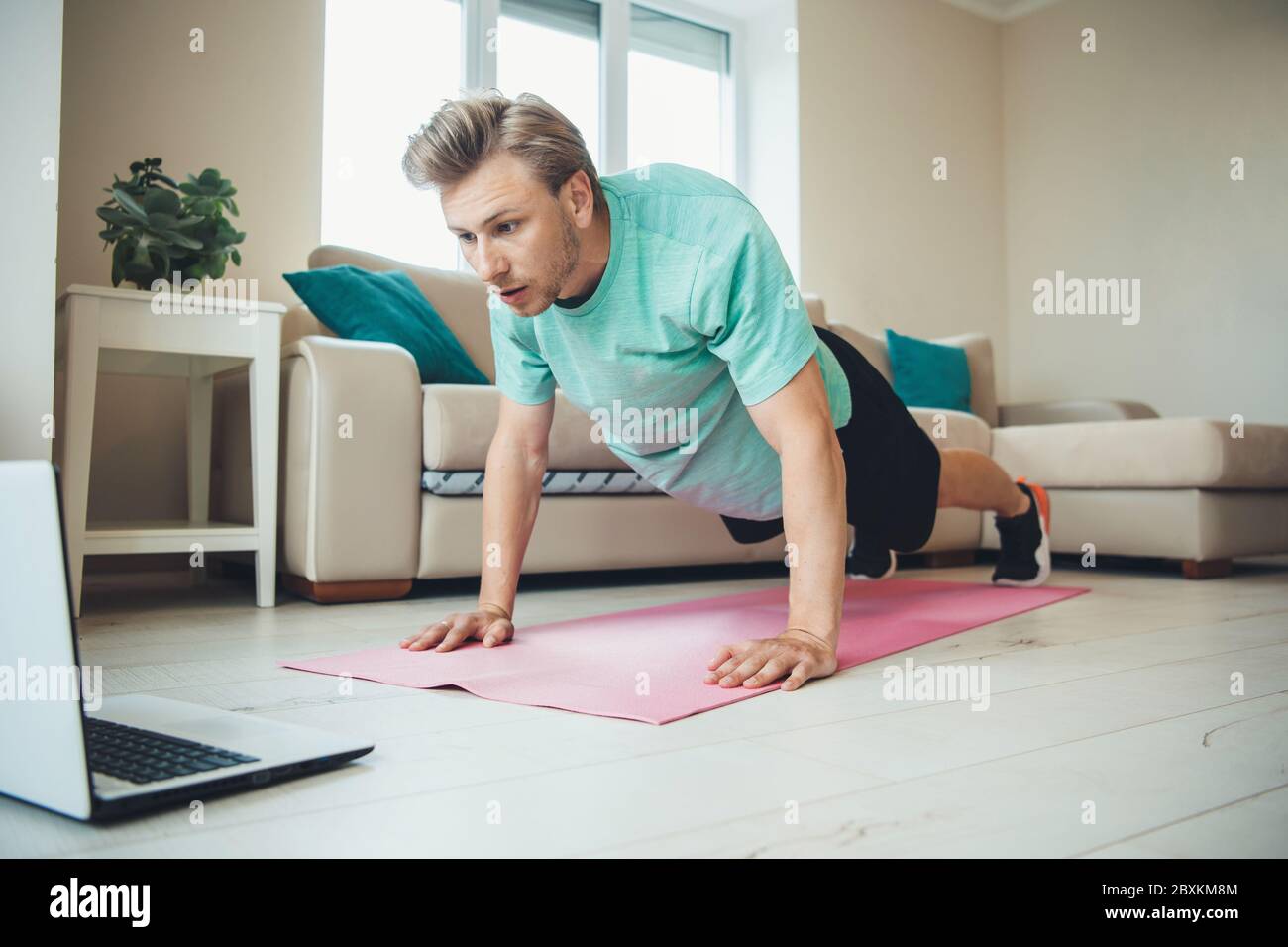 Blonde caucasian man with bristle doing push-ups on the floor using a laptop Stock Photo