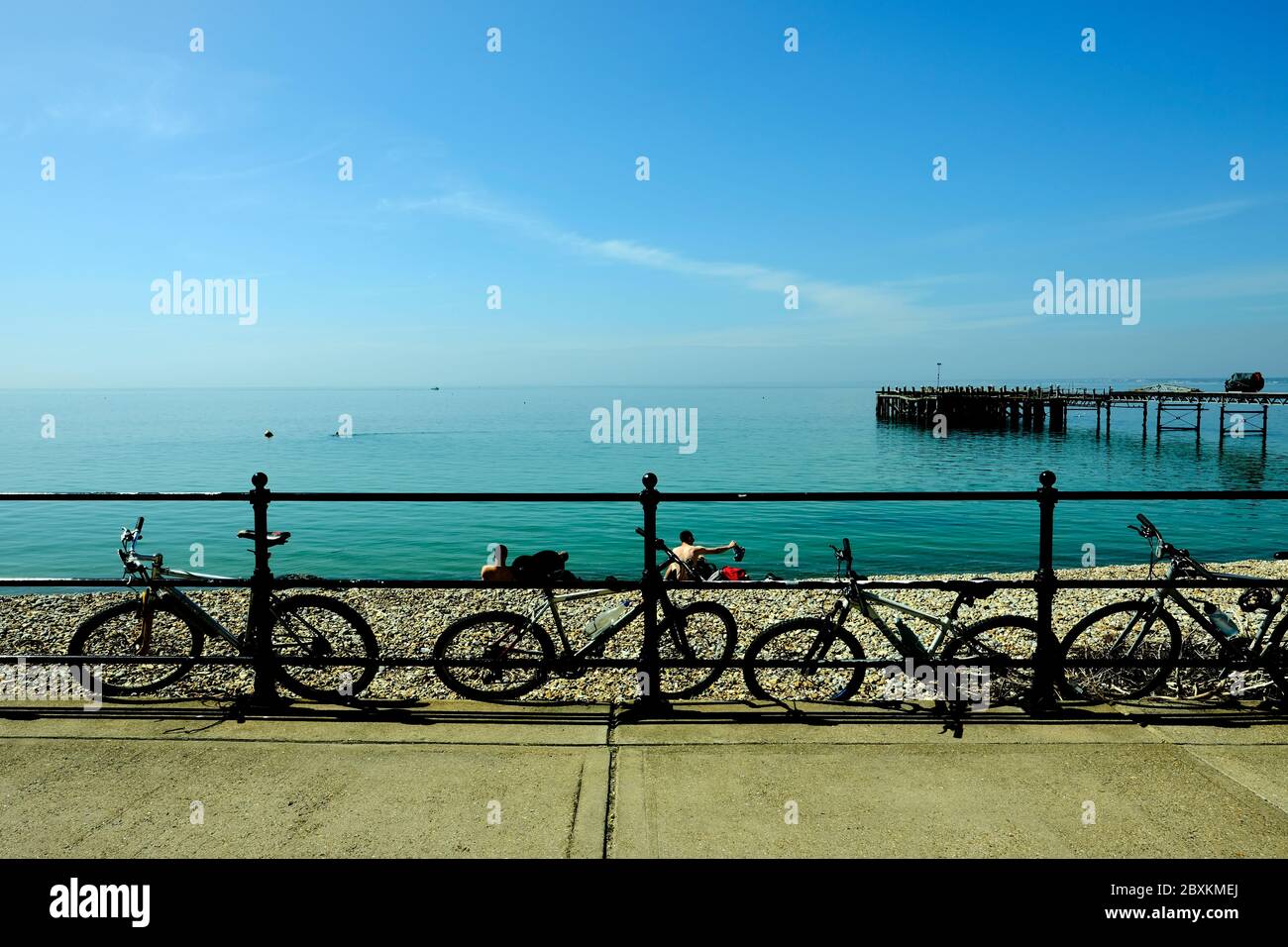 Totland Bay seafront Isle of Wight showing the old Victorian pier looking out across the Solent towards the mainland beachgoers parked bicycles Stock Photo