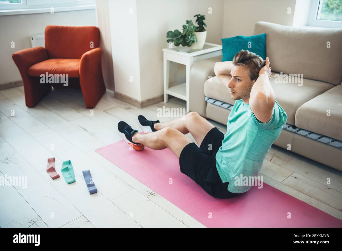 Caucasian man with bristle doing abs exercises at home on a yoga carpet using some elastic bands Stock Photo