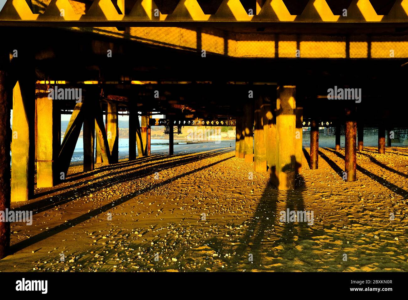 Sandown pier at sunrise low tide sun shining through under the boardwalk bright day beautiful weather long shadows of couple man and woman Stock Photo