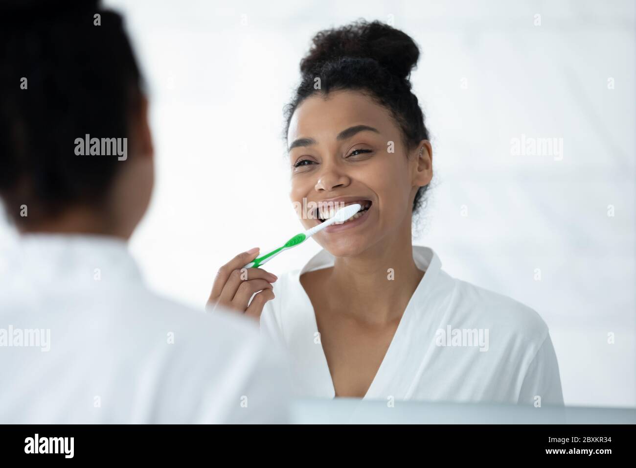 Mirror reflection smiling African American young woman brushing teeth Stock Photo