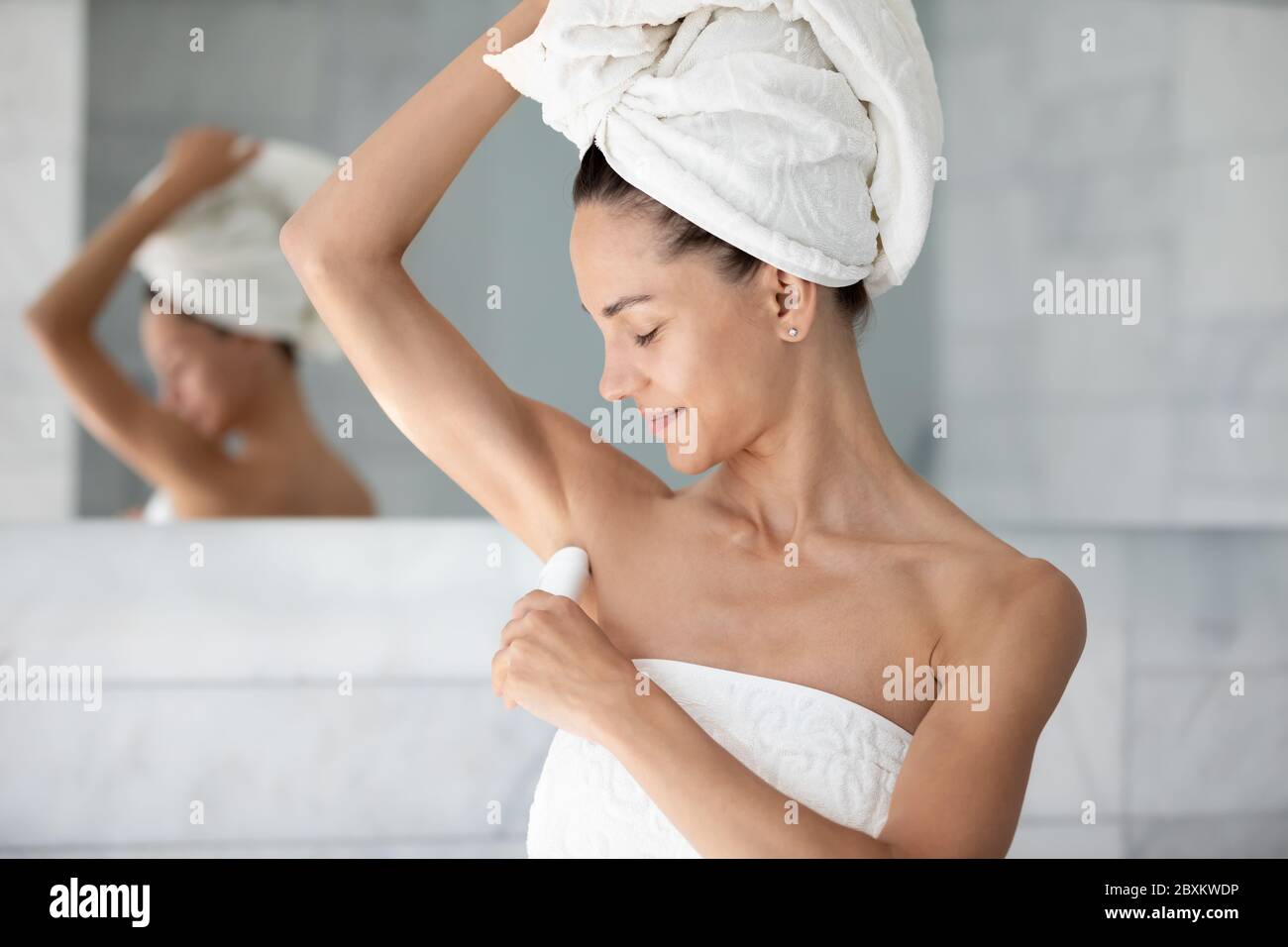 Satisfied young woman applying antiperspirant on armpit after shower