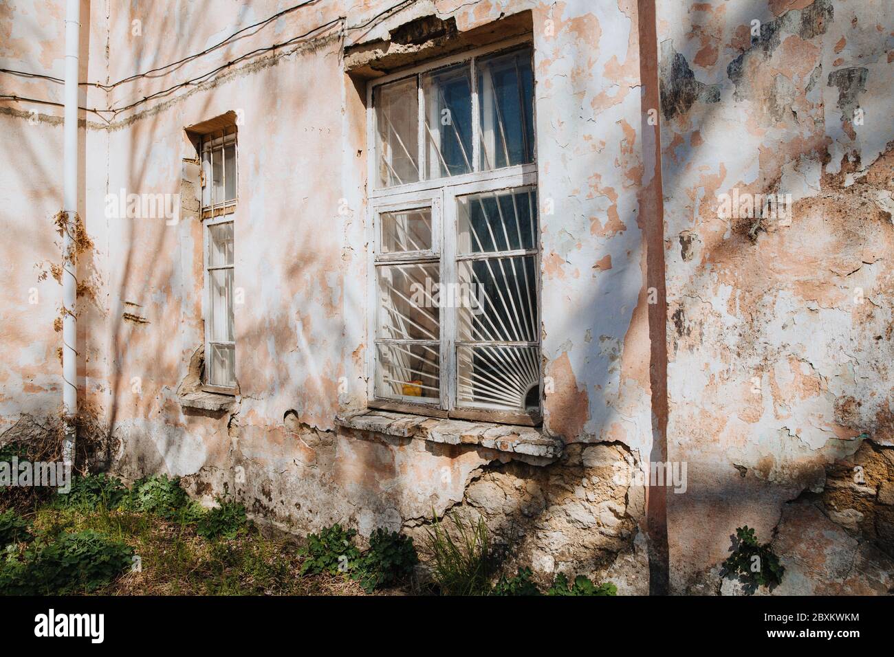 An old, crumbling window with a rusty bars on it. Damaged building. Stock Photo