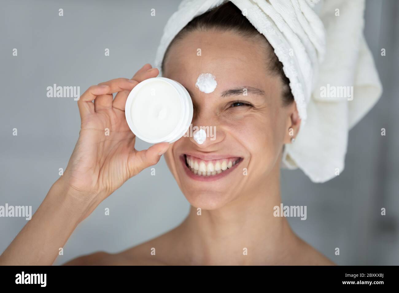 Head shot portrait smiling woman holding white face cream jar Stock Photo