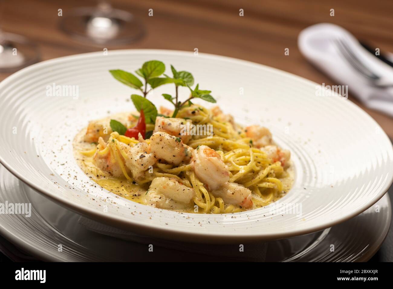 Shrimp creamy italian pasta on plate and wooden table, fork napkin leather mat and wine glasses Stock Photo