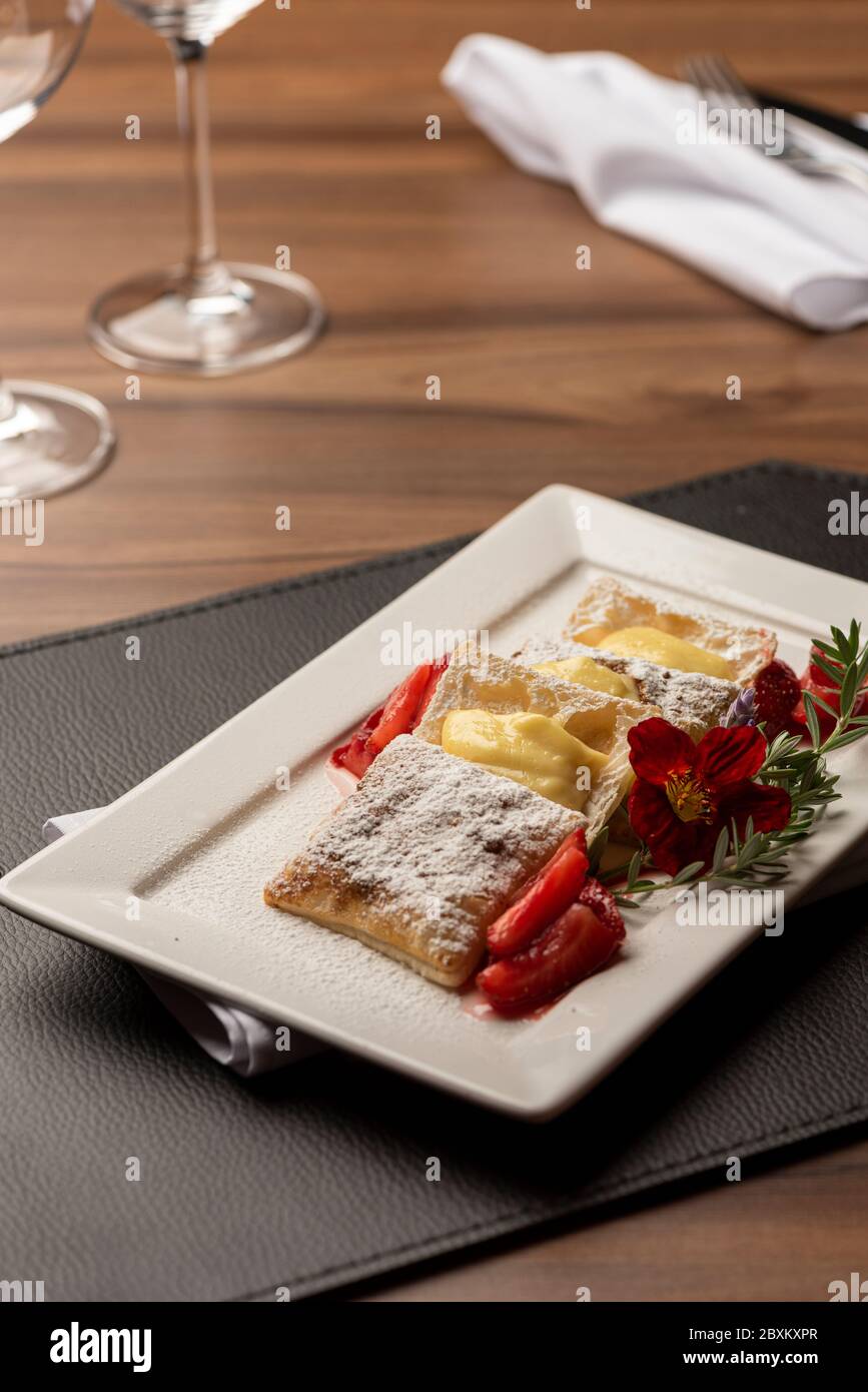 Puff Pastry with cream, strawberry and sugar on top garnished with flowers and rosemary Stock Photo