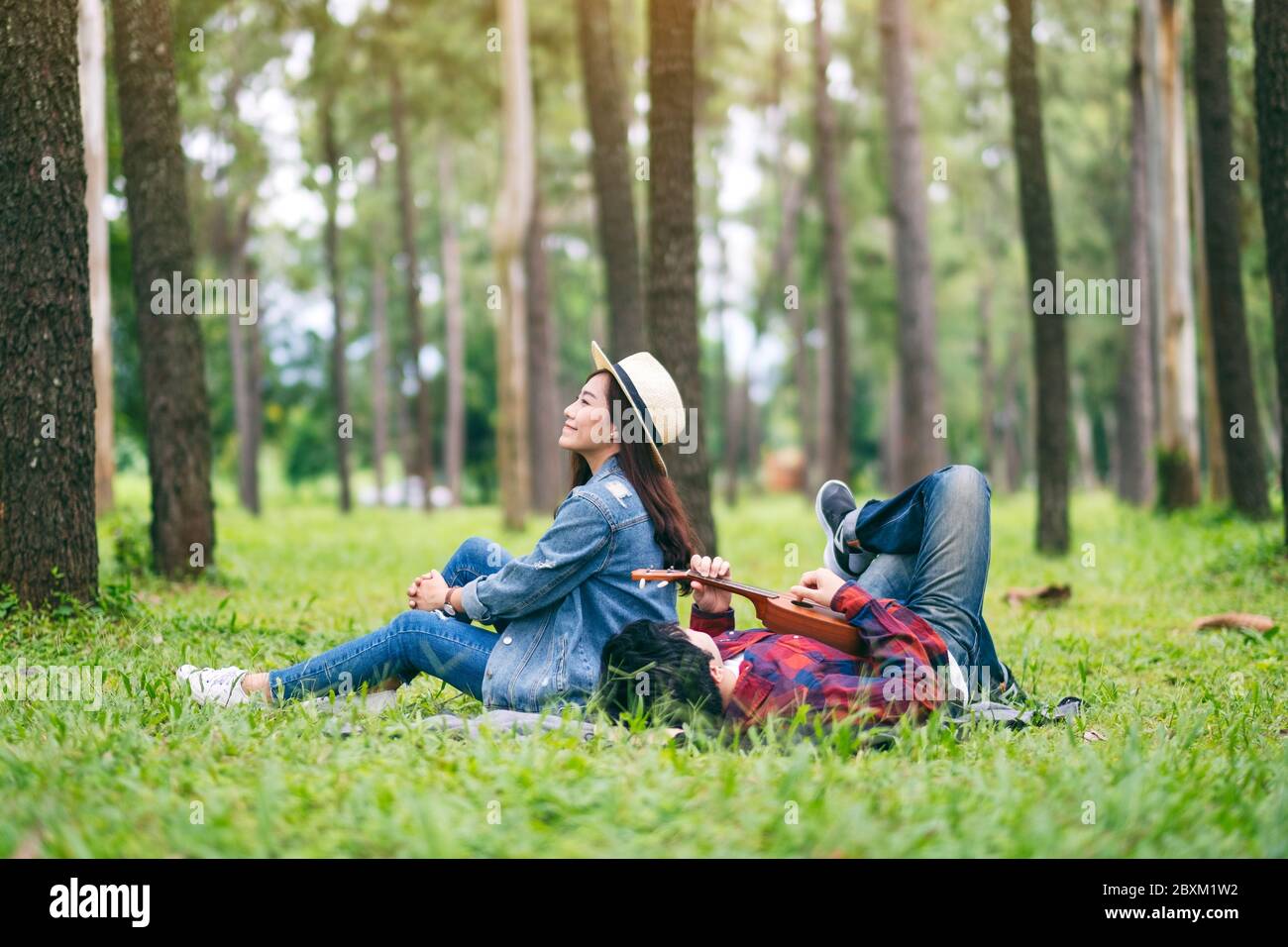 A young couple playing ukulele while sitting and lying down in the woods together Stock Photo