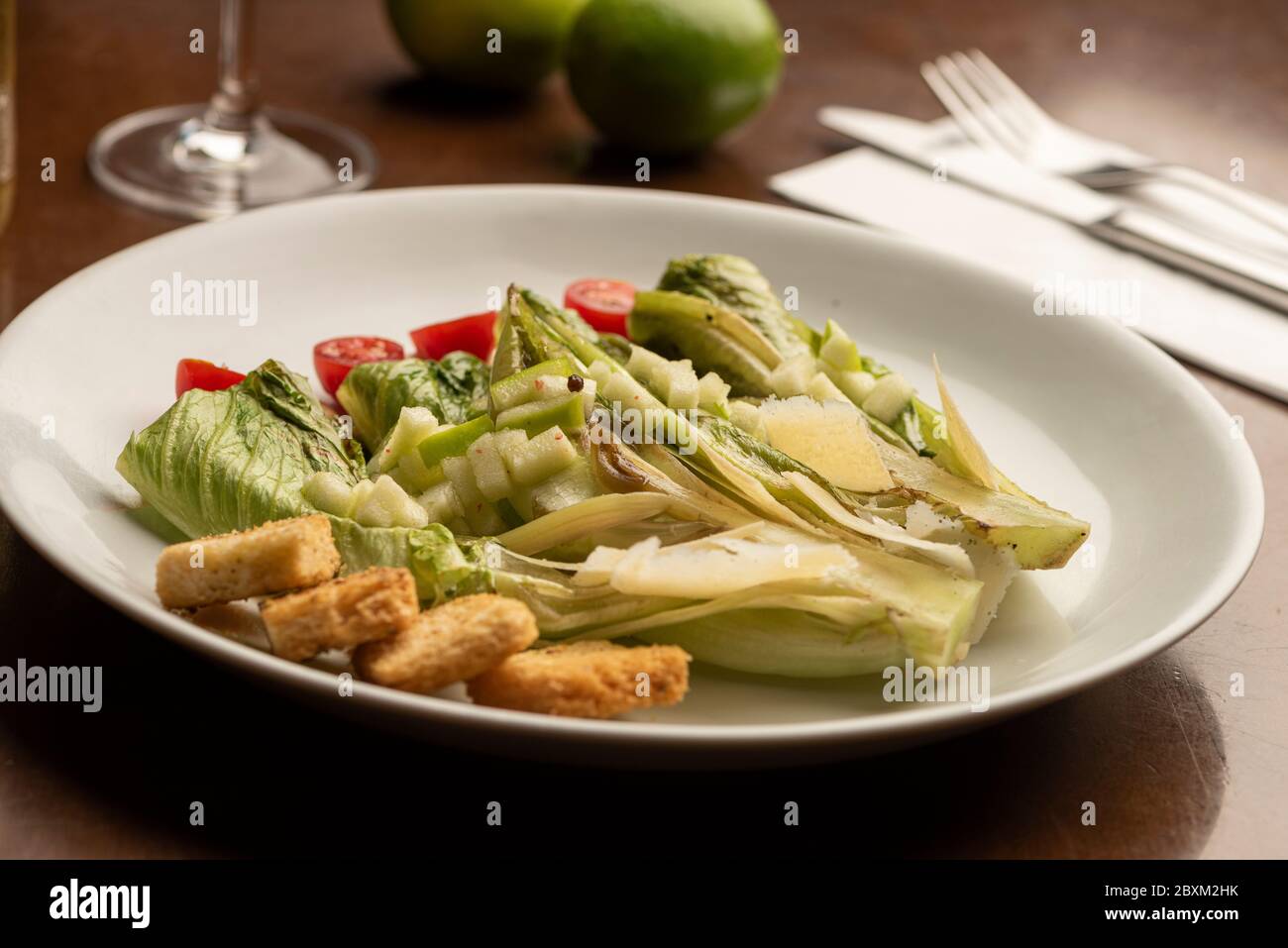 salad half cut lettuce dressing wine glass and limes on wooden table Stock Photo