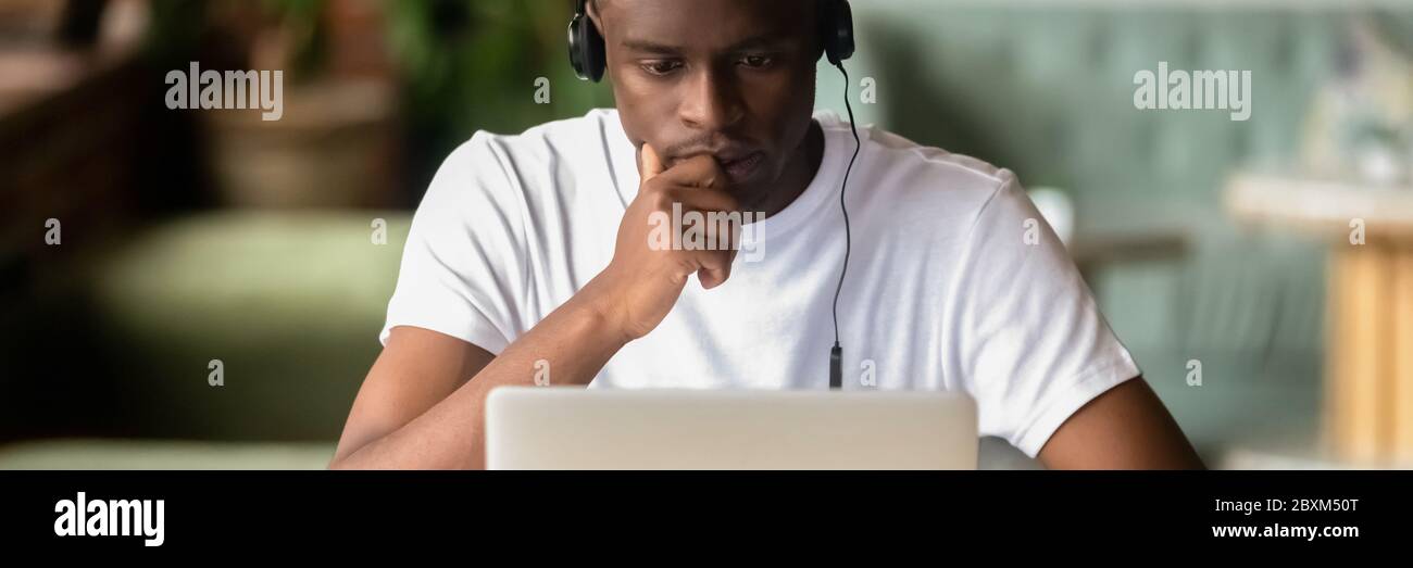 Focused African student wear headphones studying using laptop ...