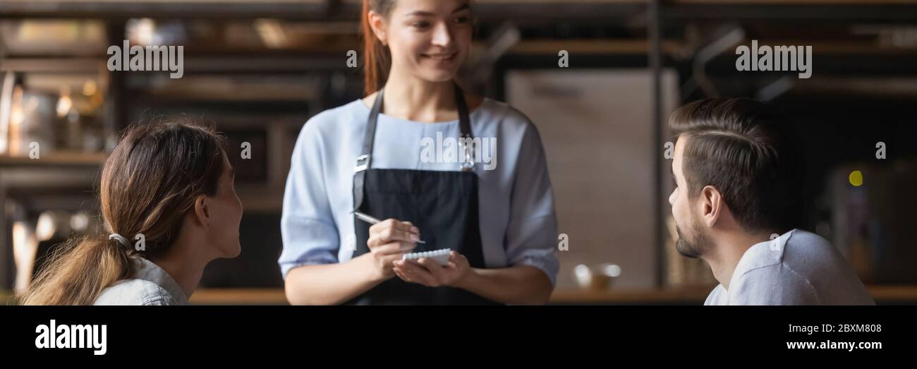 Waitress holding notepad ready take restaurant visitors couple order Stock Photo