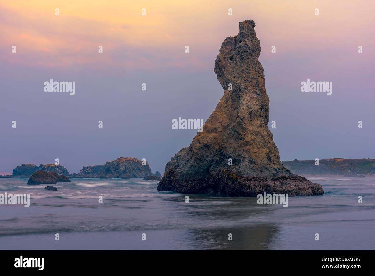 Long exposure image of waves breaking on the beach near Howling Dog Rock at sunset in Bandon, Oregon. Stock Photo