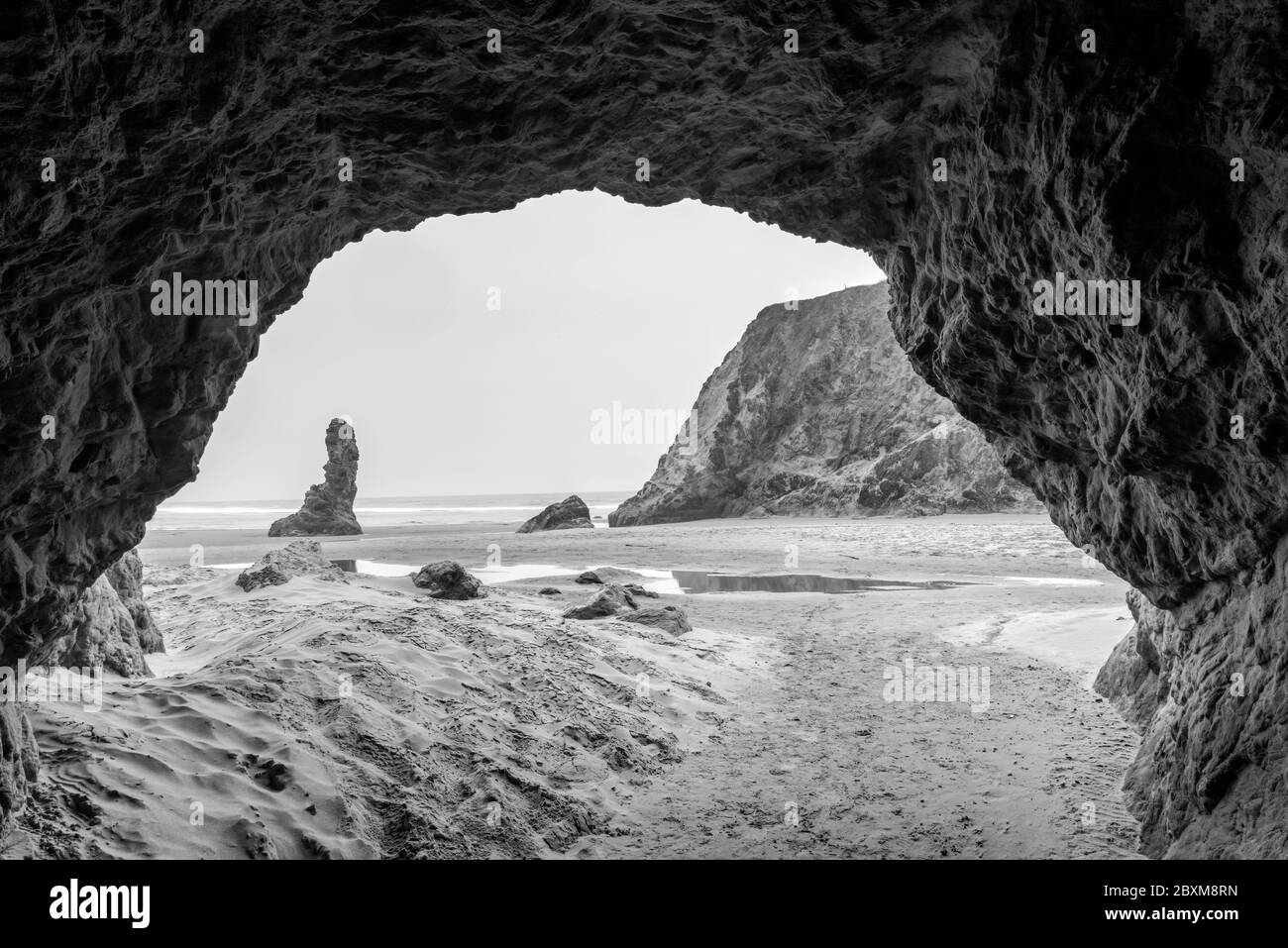 Sea cave on a beach in Bandon, Oregon opens to views of Howling Dog Rock and other sea stacks. Stock Photo