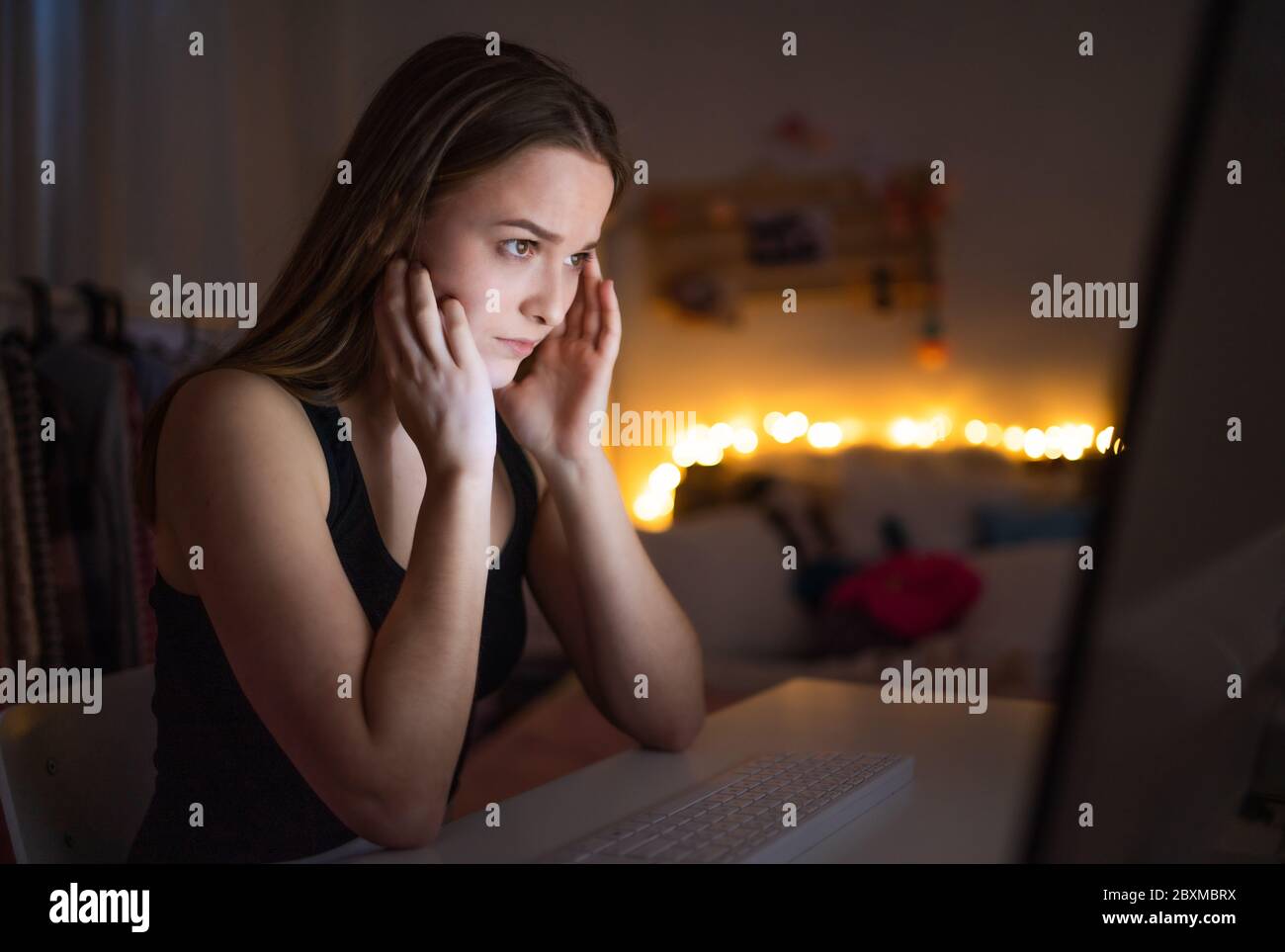 Worried young girl with computer sitting indoors, internet abuse concept. Stock Photo