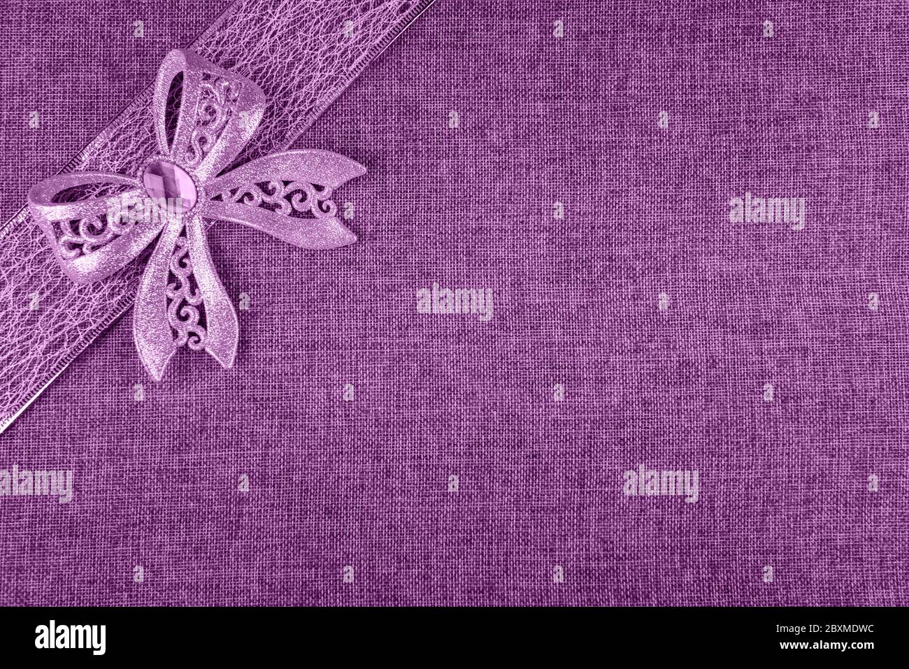 Elegant shiny lilac glitter bow on lilac colored ribbon and on lilac burlap. Horizontal greeting card background with large copy space and decorated c Stock Photo