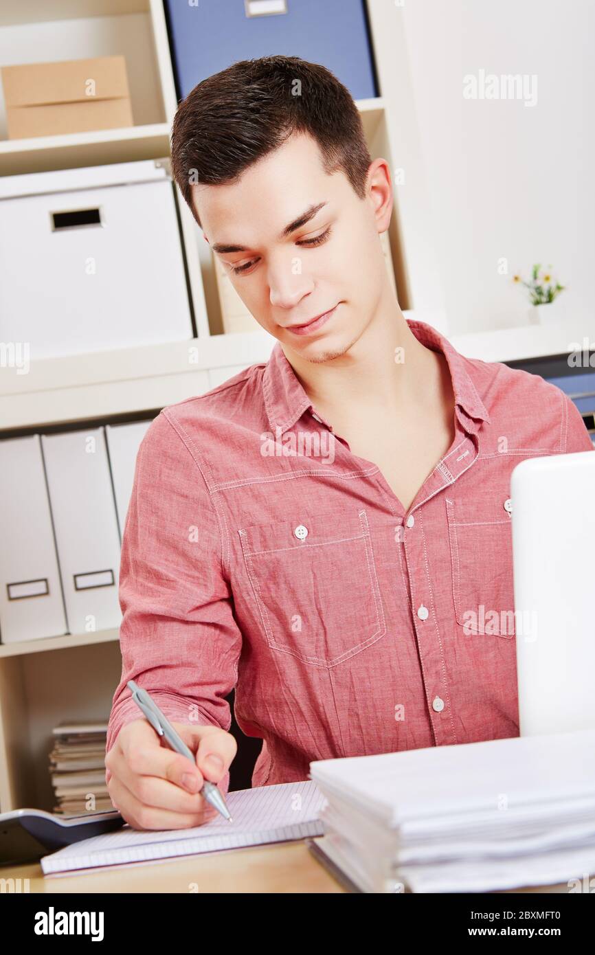 Student writes notes with pen next to the computer at the table Stock Photo