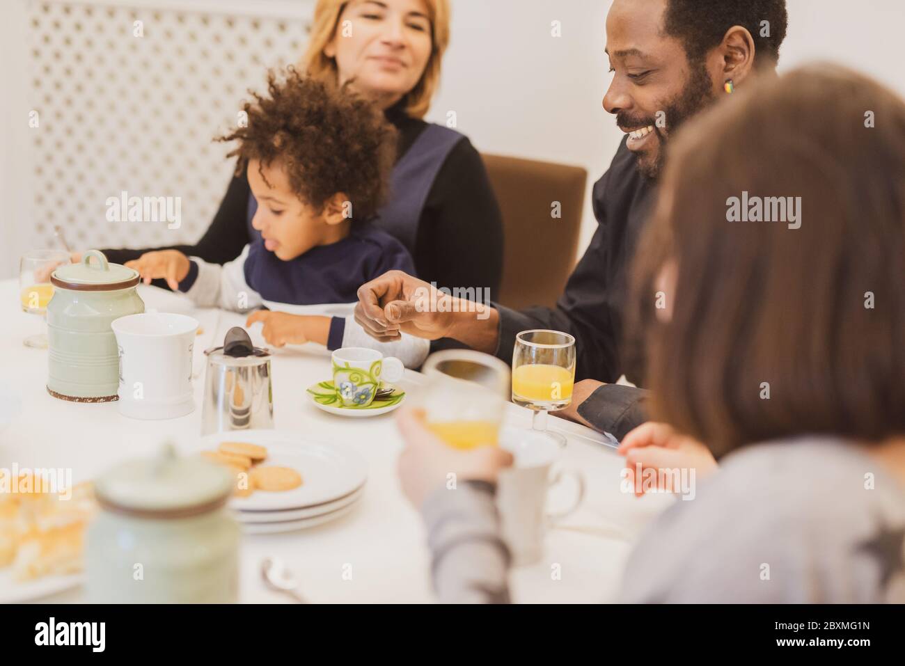 Happy interracial family with little children having breakfast in the morning, moments of daily life with Caucasian mother, African father and mixed-r Stock Photo