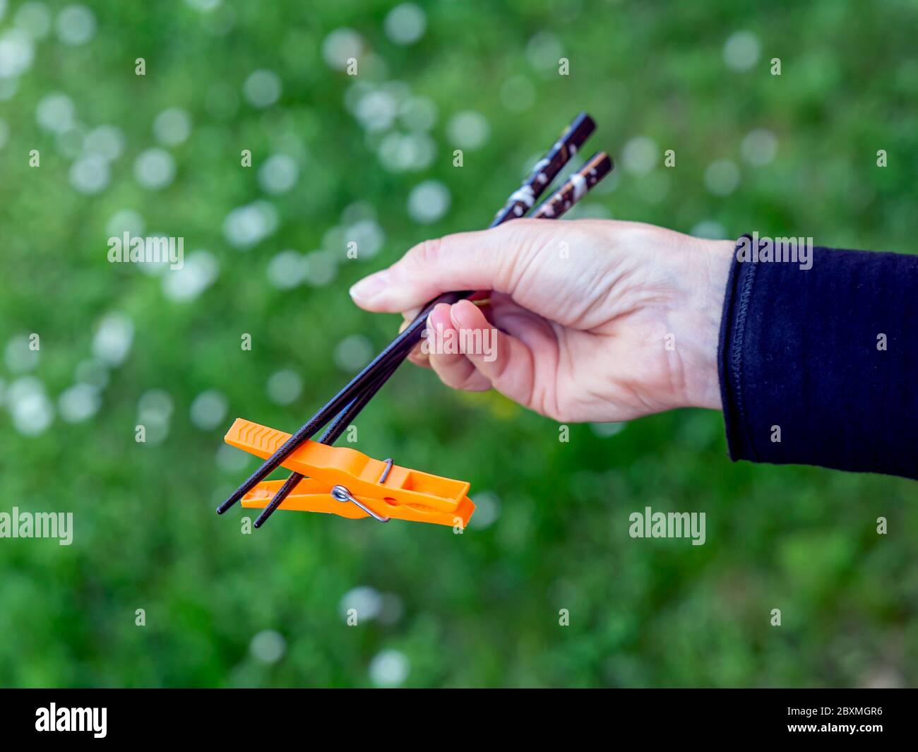 A female hand holds two Japanese chopsticks with which she raises a piece of plastic to symbolize the environmental problem Stock Photo